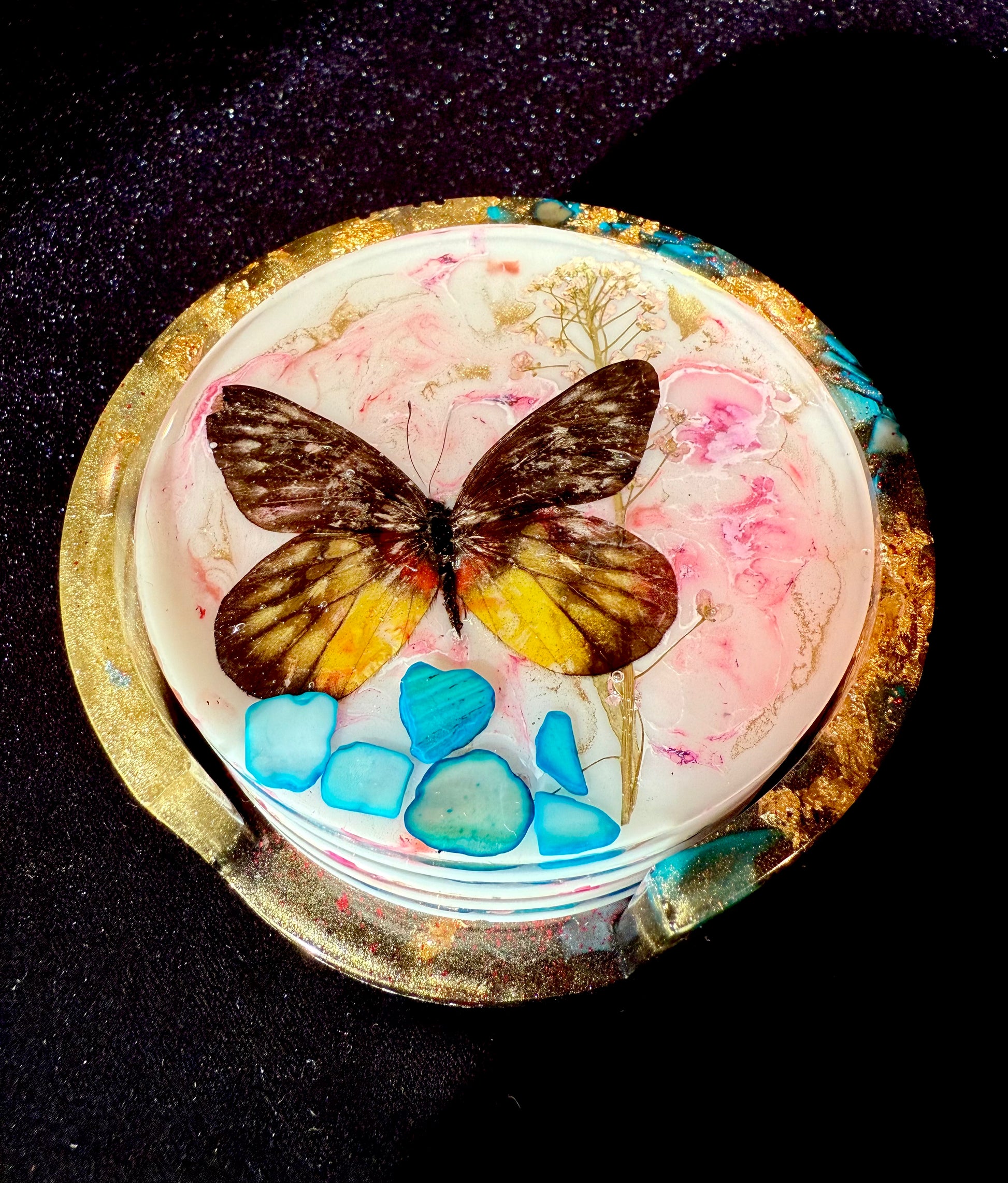 Decorative item with a butterfly, colorful stones, and a gold rim on a dark background